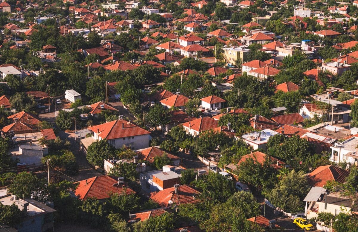 Aerial view of a residential township of red-roofed homes set among greenery and trees — Lords of the Lands