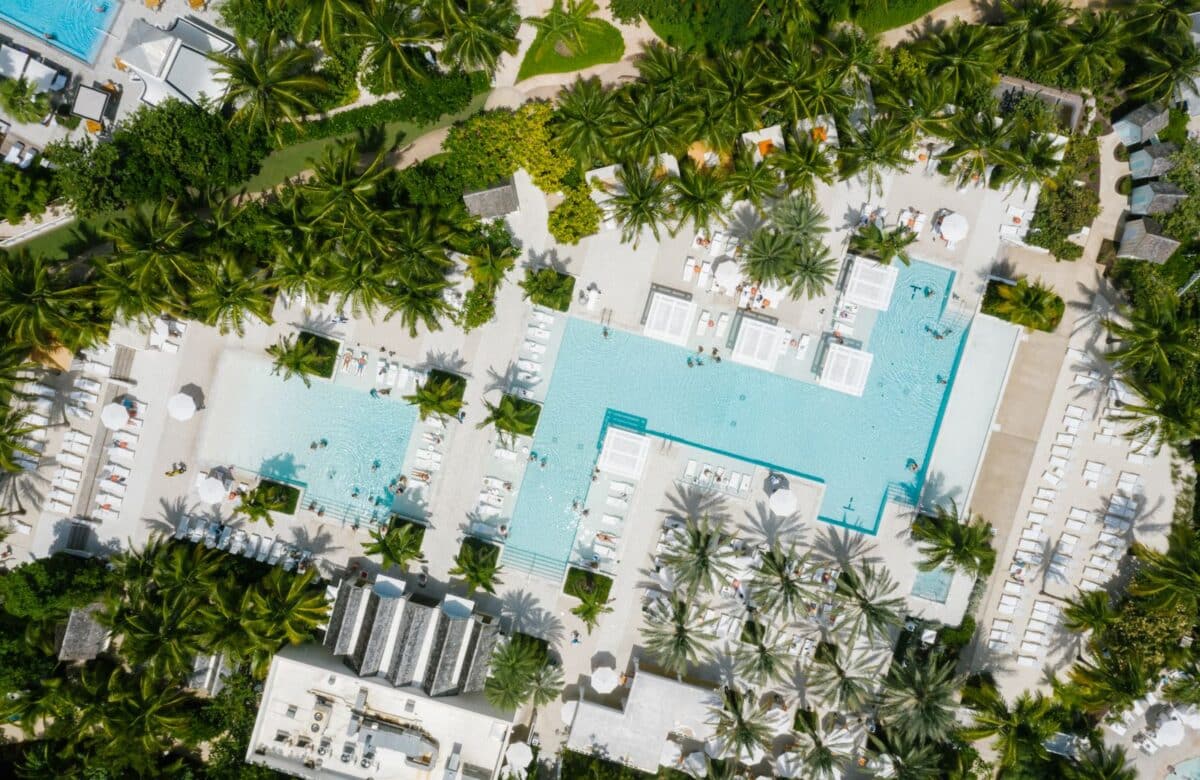 Clubhouse aerial - LORDS OF THE LANDS Aerial view of a resort clubhouse with a turquoise swimming pool surrounded by palms and landscaped gardens — Lords of the Lands