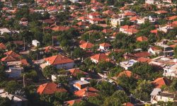Aerial view of a residential township of red-roofed homes set among greenery and trees — Lords of the Lands