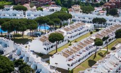 Aerial view of a white-walled villa township laid out in rows beside the coast — Lords of the Lands