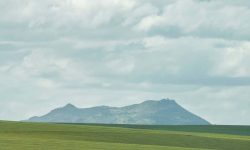 Green open field beneath a distant forested hill under a cloudy sky, Sahyadri-style landscape — Lords of the Lands