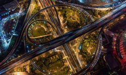 Aerial night view of a tangled, illuminated highway interchange with looping ramps and city lights below, showing busy traffic paths — Lords of the Lands
